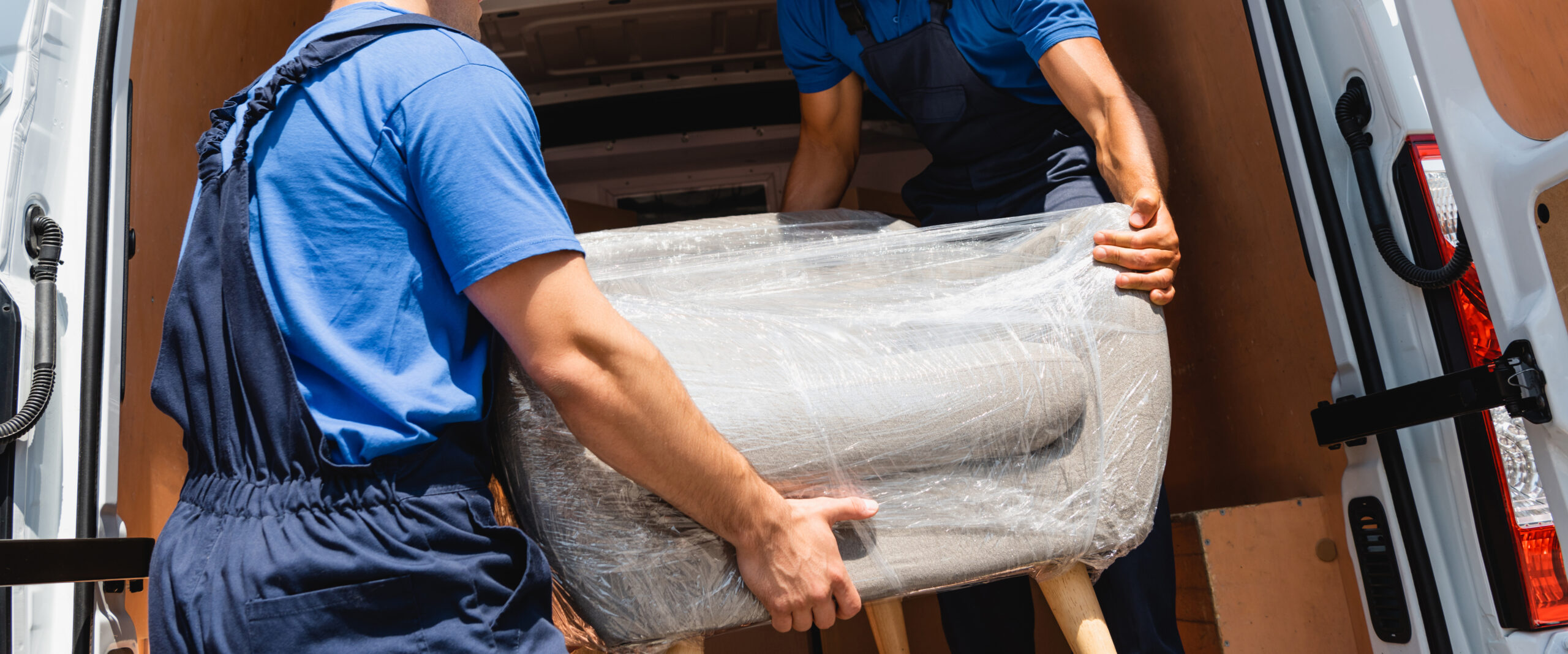 movers in uniform loading armchair in stretch wrap in truck outd